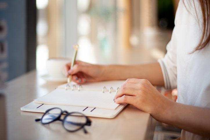 Woman creating a to-do list in a planner next to glasses
